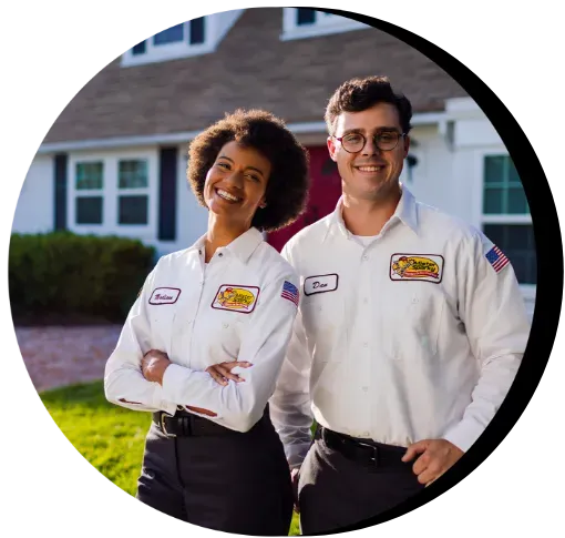 Two electricians in uniform smiling in front of a home.