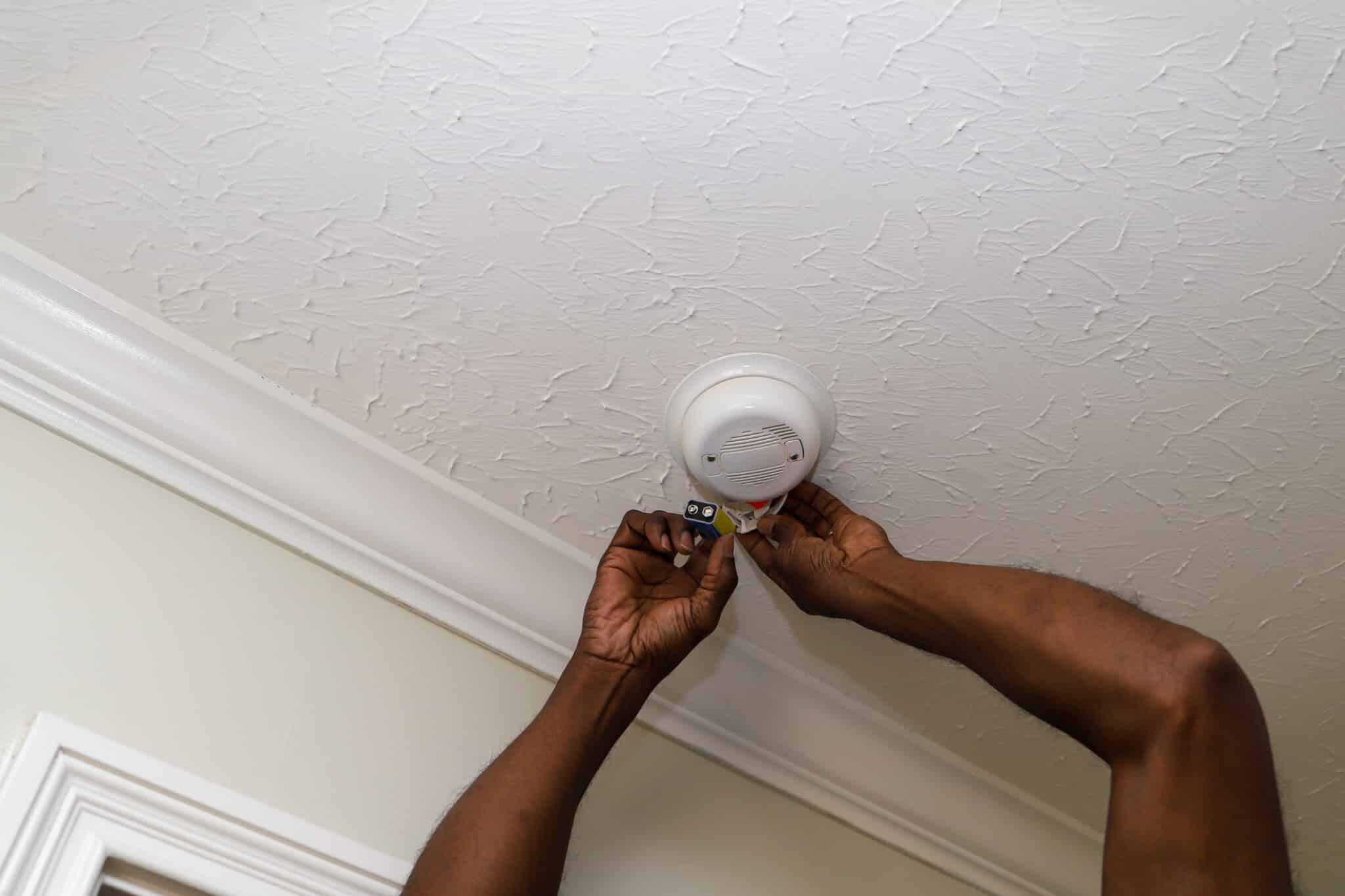 hands putting batteries in smoke detector